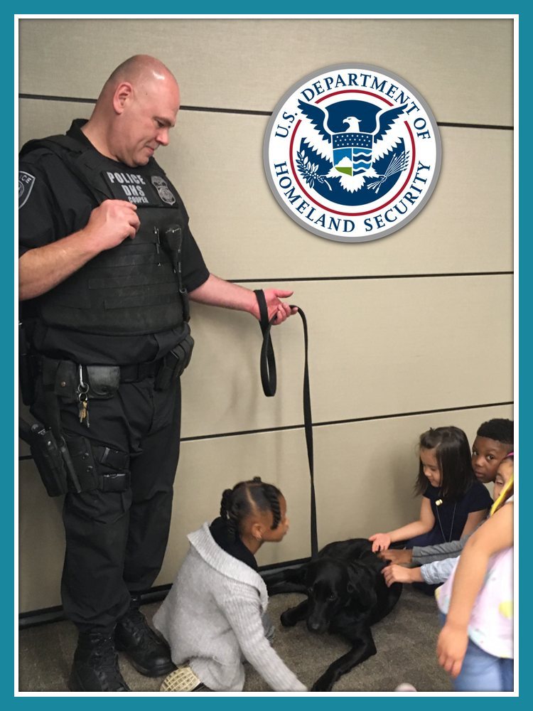 DHS officer holding dog on leash around group of children