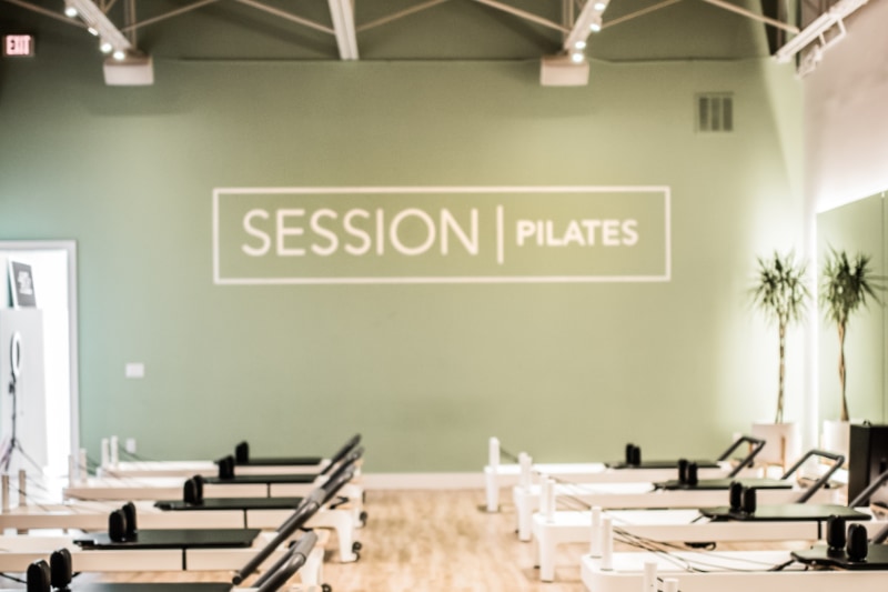 SESSION Pilates room with green walls and pilates equipment lined along floor