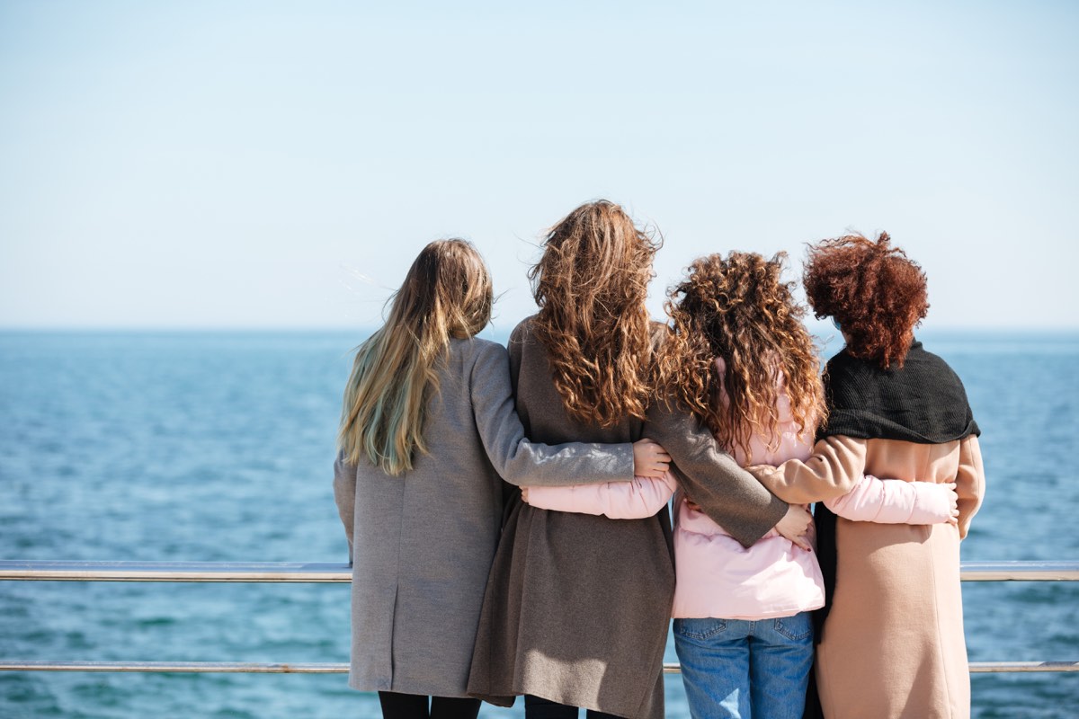 four woman hugging each other on a pier overlooking an open body of water