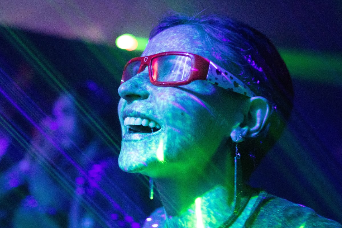 young woman with red glasses in nightclub with green and purple lights over her face and neck