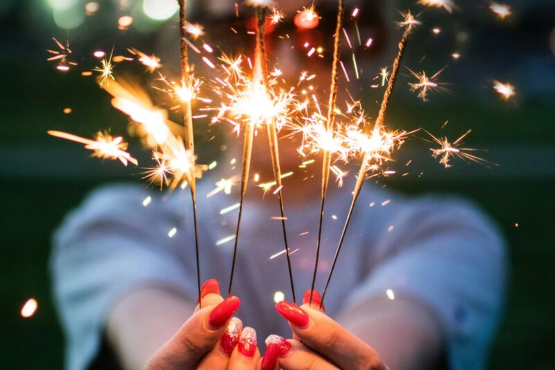 person with long red fingernails holding sparklers in front of their face